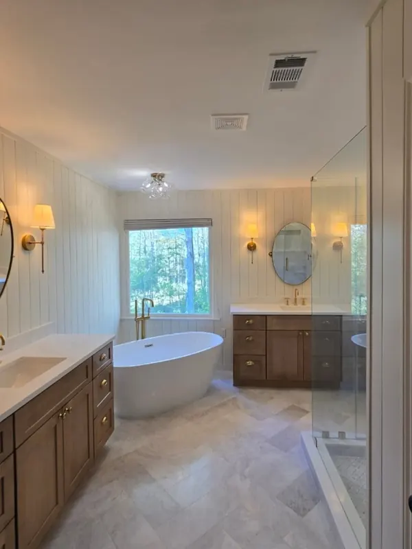 The same bathroom after, with a freestanding tub, wood vanities, paneled walls and brass fixtures