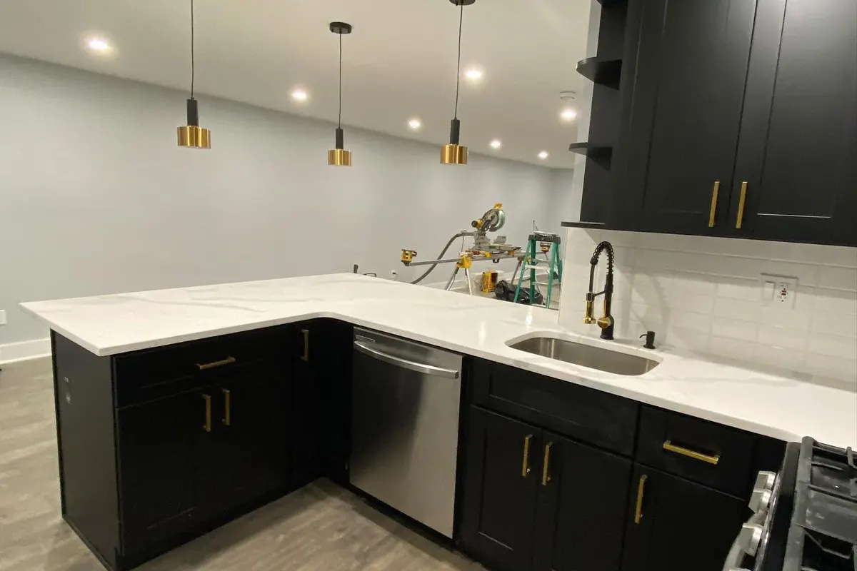 Kitchen with black shaker cabinets, gold pulls, white counters and pendant lights